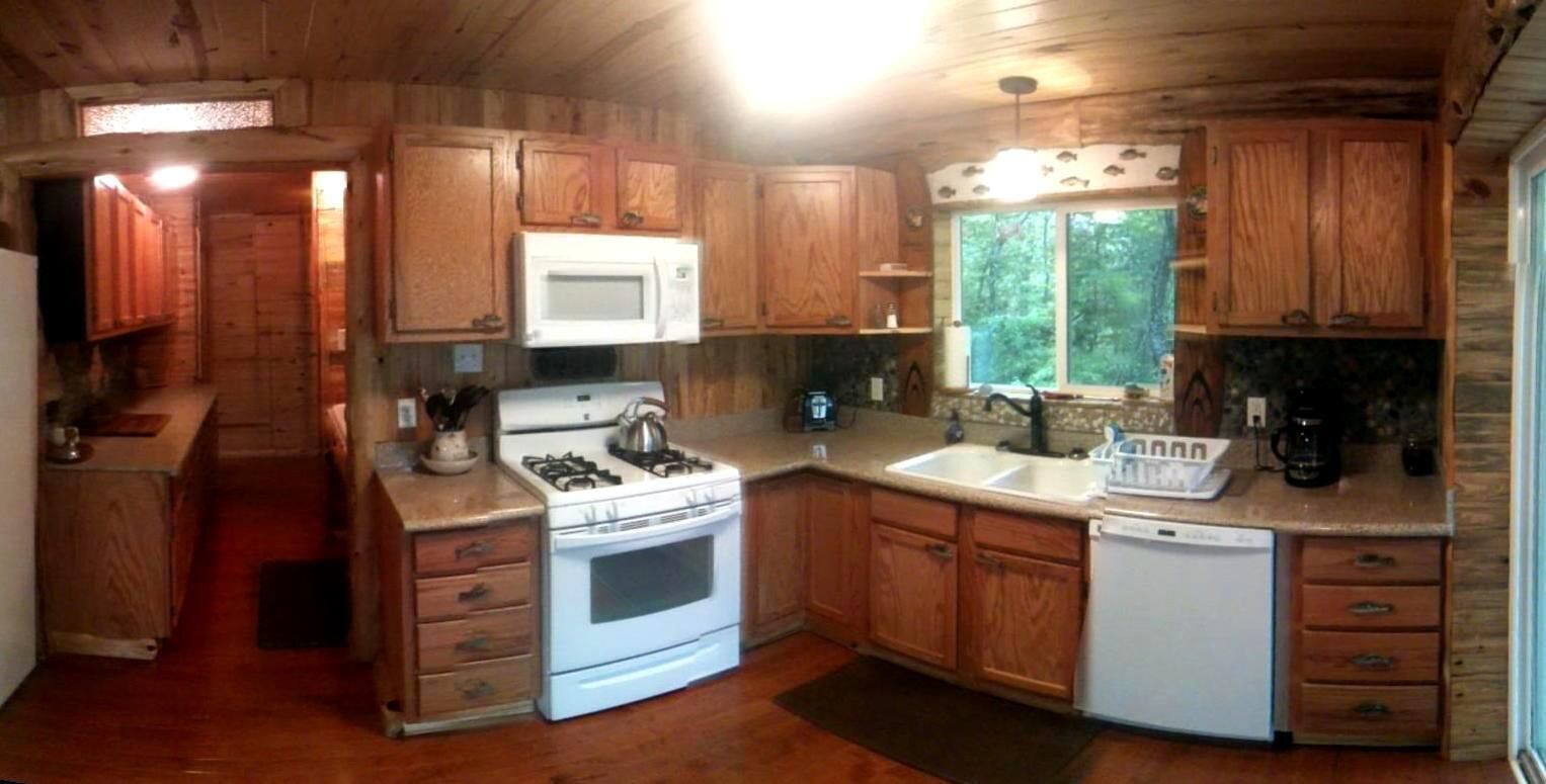 A wooden cabin kitchen with a stove, microwave, sink, and wooden cabinets.