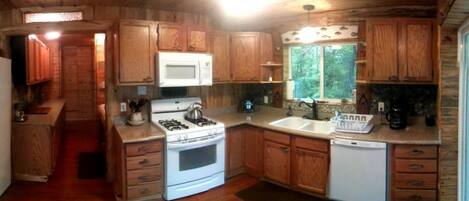 A wooden cabin kitchen with a stove, microwave, sink, and wooden cabinets.