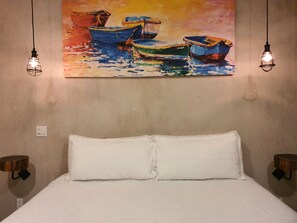 A bed with white linens, a painting of boats on the wall, and two hanging light fixtures. - Vista Tortuga - VILLA ARENA Heated Pool by the BEACH (Todos Santos)