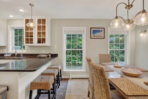 Una cocina con una isla central, taburetes de bar, sillas de mimbre y una mesa de comedor con manteles individuales.