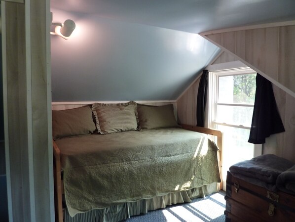 A bedroom with a bed, a window, and a wooden dresser.