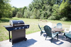 An outdoor patio with a grill, chairs, and a table. - All Season Camp for Your Adirondack Adventures, 5 miles to Whitetace Mountain (Wilmington)