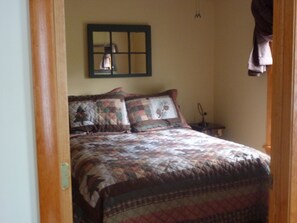 A bedroom with a large bed, a nightstand, a lamp, and a framed picture on the wall. - All Season Camp for Your Adirondack Adventures, 5 miles to Whitetace Mountain (Wilmington)