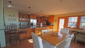 A spacious kitchen with wooden cabinets, a dining area with a wooden table and white chairs, and a cozy seating area with wicker furniture. - Waterfront, beautiful home, breathless sunsets on Prudence Island (Prudence Island)