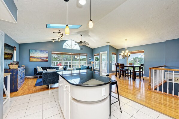 A spacious kitchen with a central island, a dining area with wooden chairs, and a living room with a sofa and a large window. - Across the street from the Beach, restaurants, free wifi. (Holmes Beach)