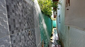 A narrow alley with a water feature, a green fence, and a building with a tiled exterior. - JUQUEHY MIDDLE OF THE BEACH, 80 METERS FROM THE SEA. (São Sebastião)