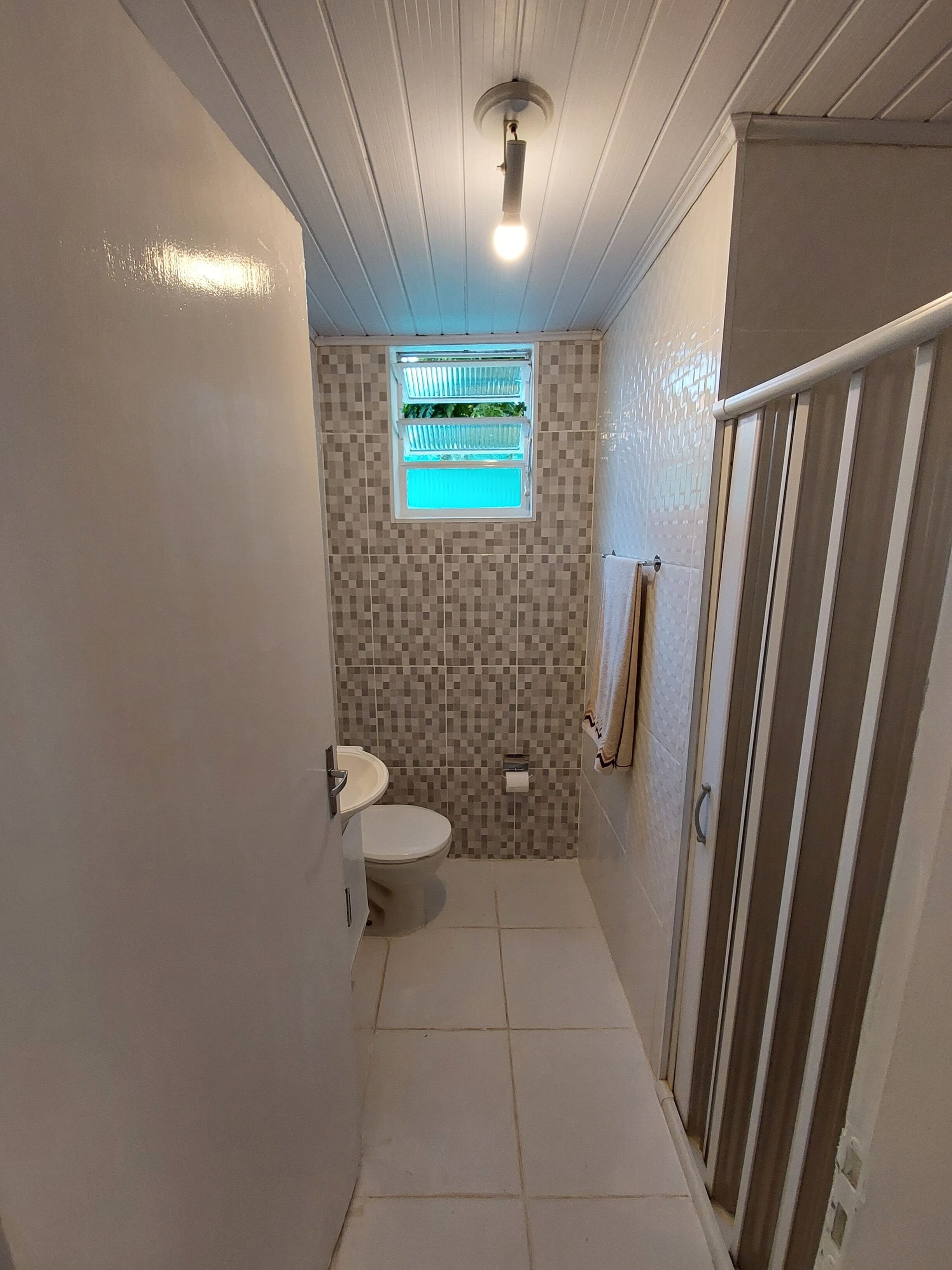 A narrow bathroom with a toilet, sink, and shower area.