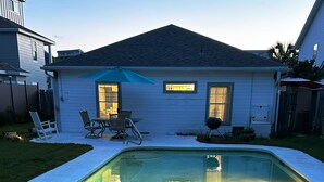 Ein rechteckiger Pool mit einer gefliesten Kante, umgeben von einer Betonplattform. Im Hintergrund sind Liegestühle und ein Grill zu sehen.