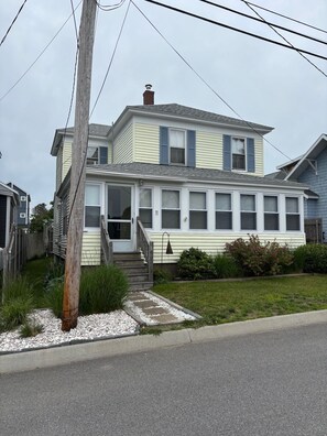 A two-story house with a front porch, a visible chimney, and a small garden area with a pathway leading to the entrance.