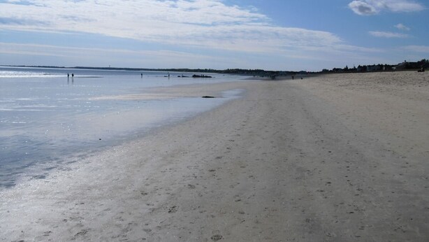 Une vaste plage de sable fin, sous un ciel dégagé parsemé de quelques nuages.