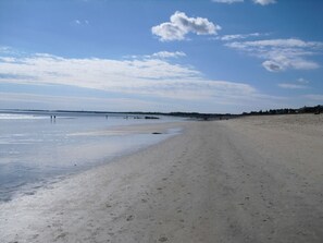 A wide, sandy beach with a clear sky and a few clouds.