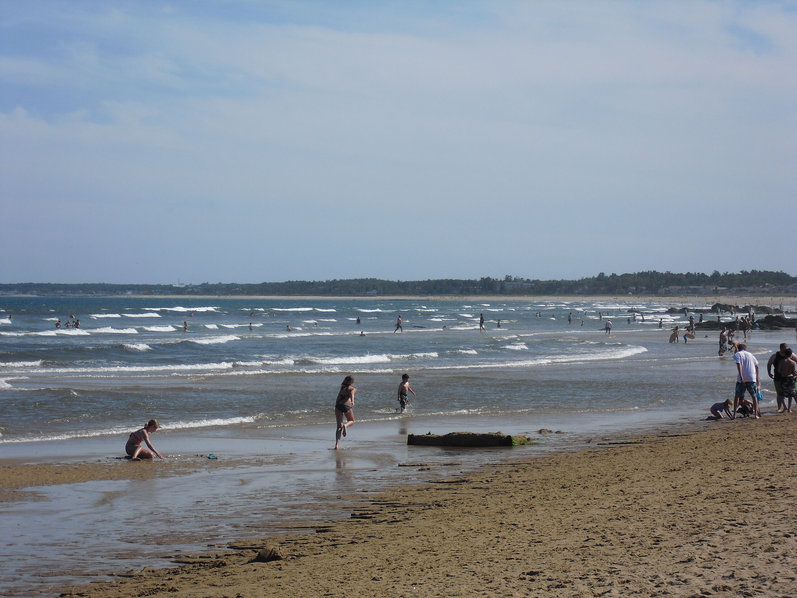 A beach with people engaging in various activities like swimming and walking.