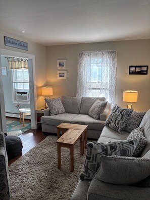 A living room with a sofa, two side tables, a rug, and a window with curtains.