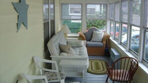 Une véranda avec deux chaises blanches, un canapé en osier et une chaise à bascule en bois.