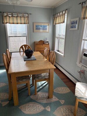Un comedor con una mesa y sillas de madera, un tapete con motivos de peces y un ventanal con vistas al exterior.