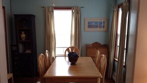 Une salle à manger avec une table en bois, six chaises, un tapis à motifs floraux, une bibliothèque et un tableau accroché au mur.
