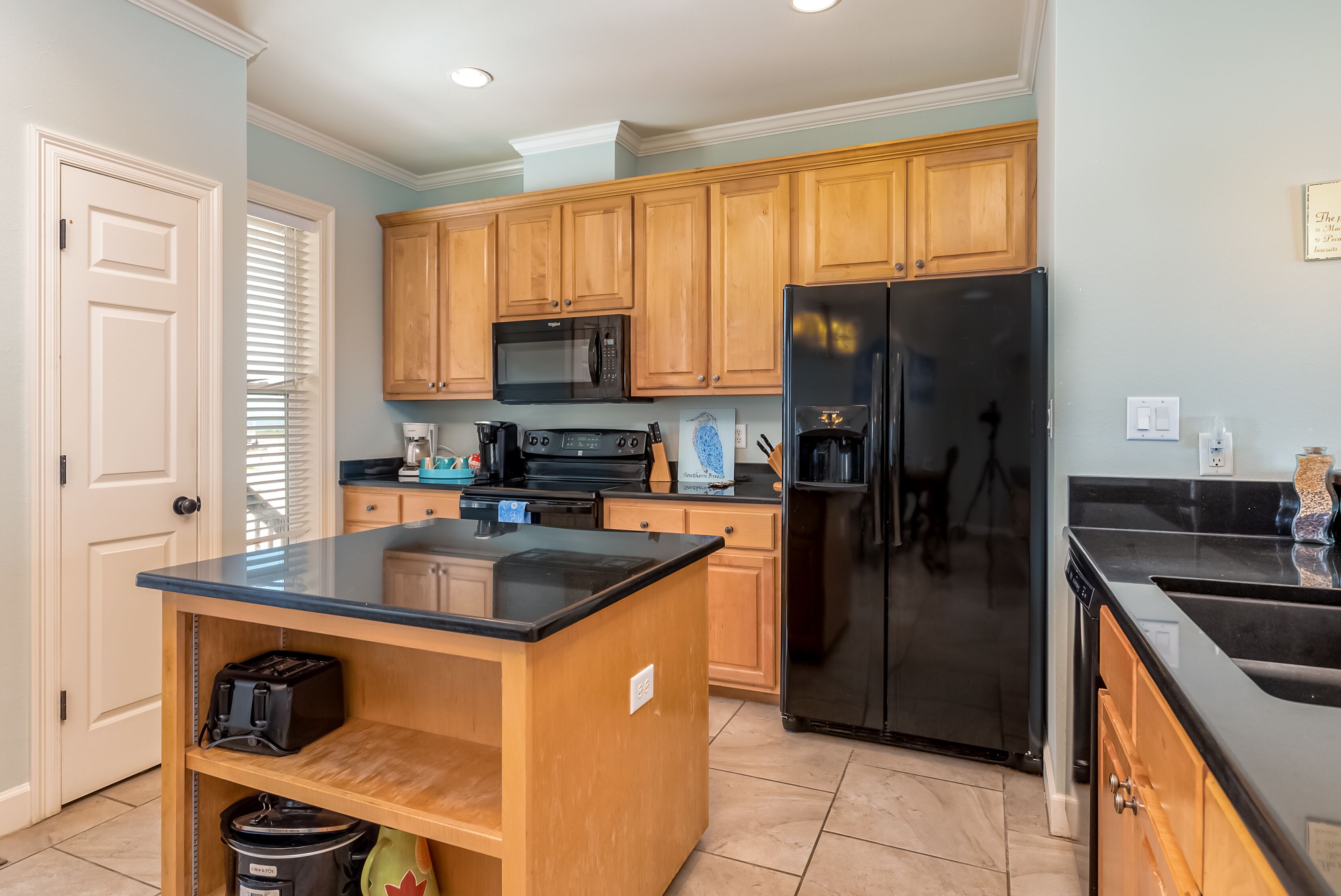 A kitchen with wooden cabinets, a black refrigerator, a microwave, and a coffee maker.