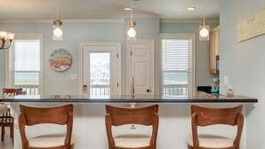 A kitchen with a central island, wooden chairs, pendant lights, and a view of the outside. - Beautiful Gulf Front home at the waves - Southern Breeze (Dauphin Island)