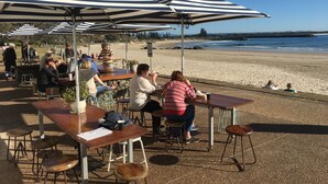 Un espace extérieur aménagé avec des tables et des parasols à rayures, donnant sur une plage.