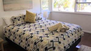 Une chambre à coucher avec une couvre-lit à motifs, des oreillers, une serviette enroulée et un tableau représentant une scène de plage.