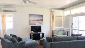 Un salon avec deux canapés gris, un téléviseur posé sur un meuble et un ventilateur de plafond.