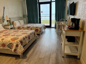 A hotel room with two beds, a desk with a coffee maker, a TV, and a view of the ocean. - Oceanfront Studio 1st floor- Pools Open - Hawaiian Inn (Daytona Beach Shores)