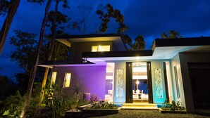 Een modern huis met een goed verlichte ingang, omringd door bomen en een tuin.