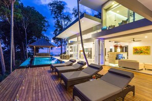 Et moderne hus med swimmingpool, liggestole og en stue med glasfacade.
