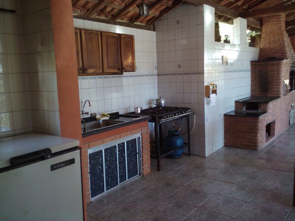 A kitchen with wooden cabinets, a tiled backsplash, a gas stove, and a brick oven. - Great farm close to São Paulo for your leisure safe and cozy place (Alumínio)