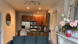 Ein Wohnzimmer mit grauem Sofa, Kamin und einer Küche im Hintergrund.