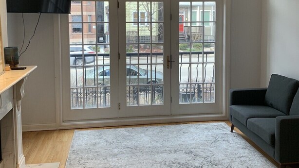 Ein Wohnzimmer mit Deckenventilator, einem flachbildfernseher an der Wand, einem dunklen Sofa und einer großen Schiebeglasdoor zum Außenbereich.