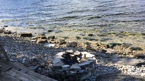 A rocky shoreline with a stone fire pit and wooden deck. - Gray Gull Cottage-Waterfront Home (Sturgeon Bay)