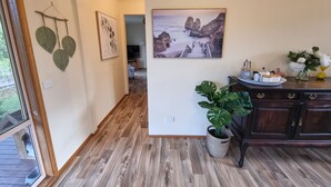 Un couloir au plancher de bois, un coin repas avec une table dressée pour deux personnes, et un grand tableau représentant un paysage côtier.