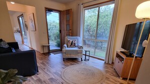 Un salon spacieux avec une grande fenêtre, un canapé, un fauteuil avec un coussin, un téléviseur et une plante en pot.