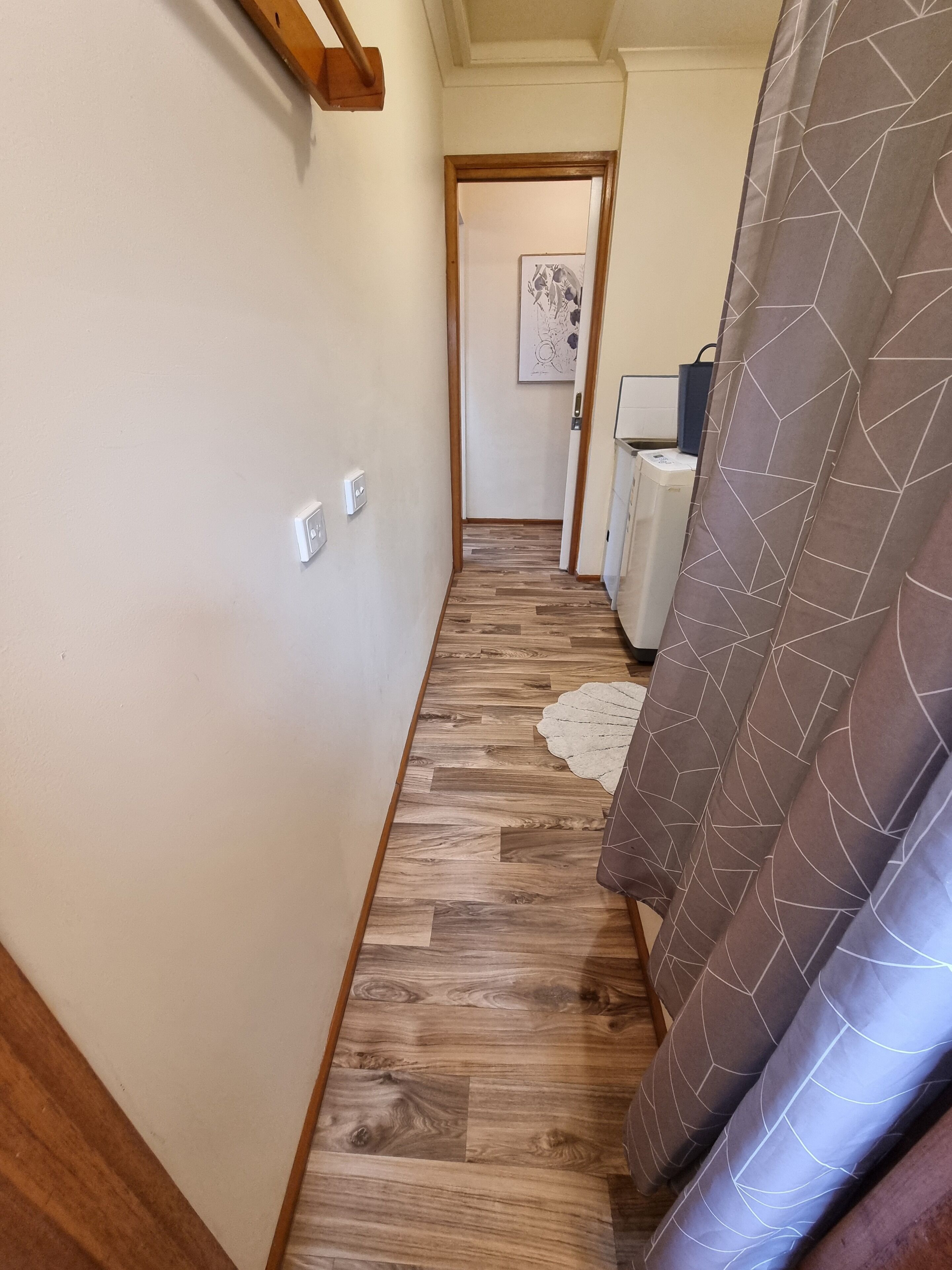 Um corredor estreito com piso de madeira, uma porta no final e um luminário fixado na parede.