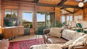 A wooden cabin interior with a leather sofa, a television, and a dining area with chairs. - Easter Weekend Special, 20% off! Insider tip Easter egg hunt at the beach! (Manchester)