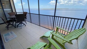 A balcony with a view of the sea, a table with chairs, and a sign on the floor. - Sanibel Harbour Resort732: Experience dolphin tours by day and sunset views from your private lanai. (Fort Myers)