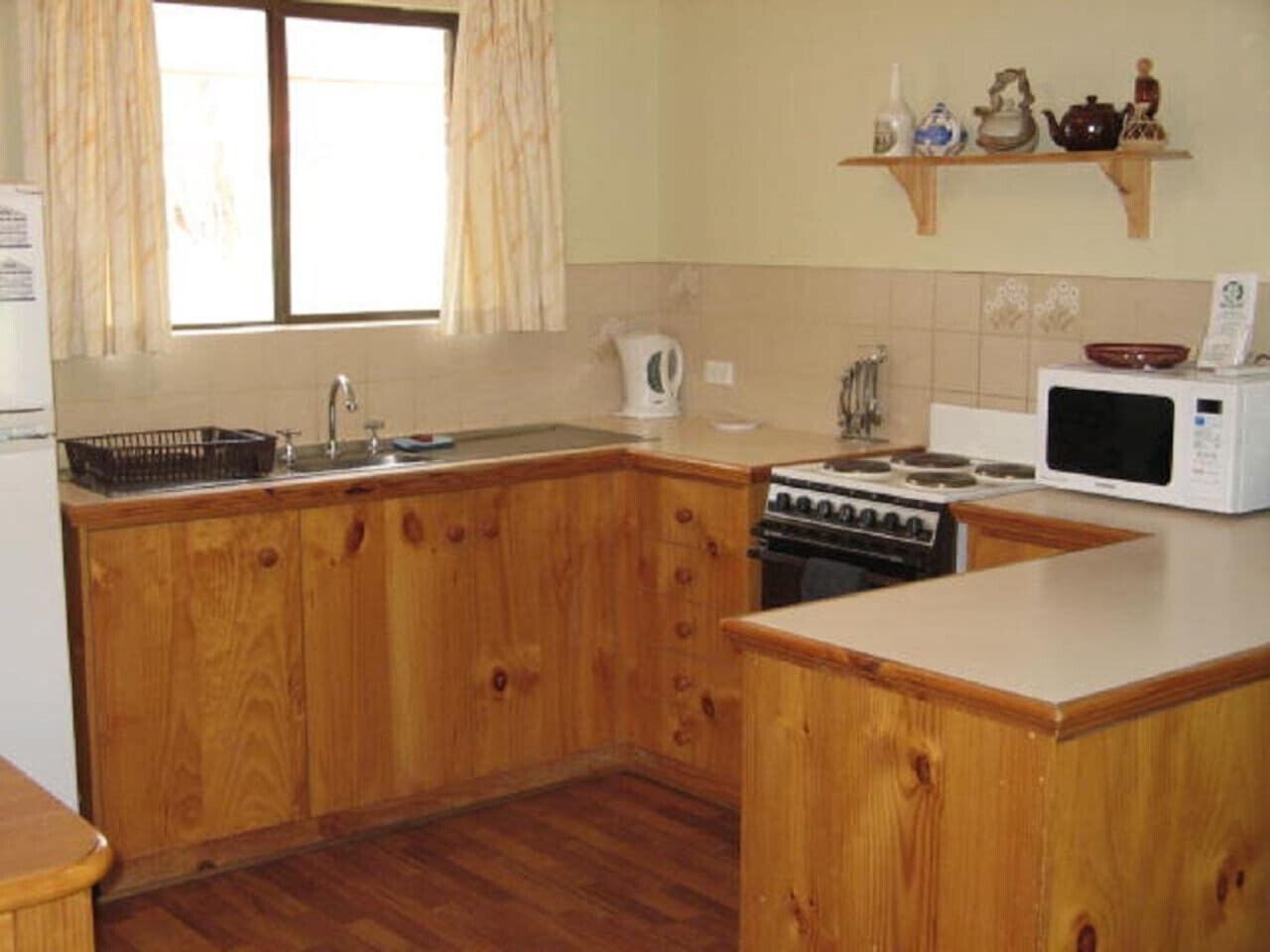 A kitchen with wooden cabinets, a stove, a microwave, and a window with curtains.