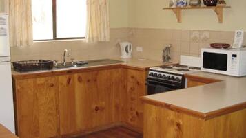 A kitchen with wooden cabinets, a stove, a microwave, and a window with curtains.