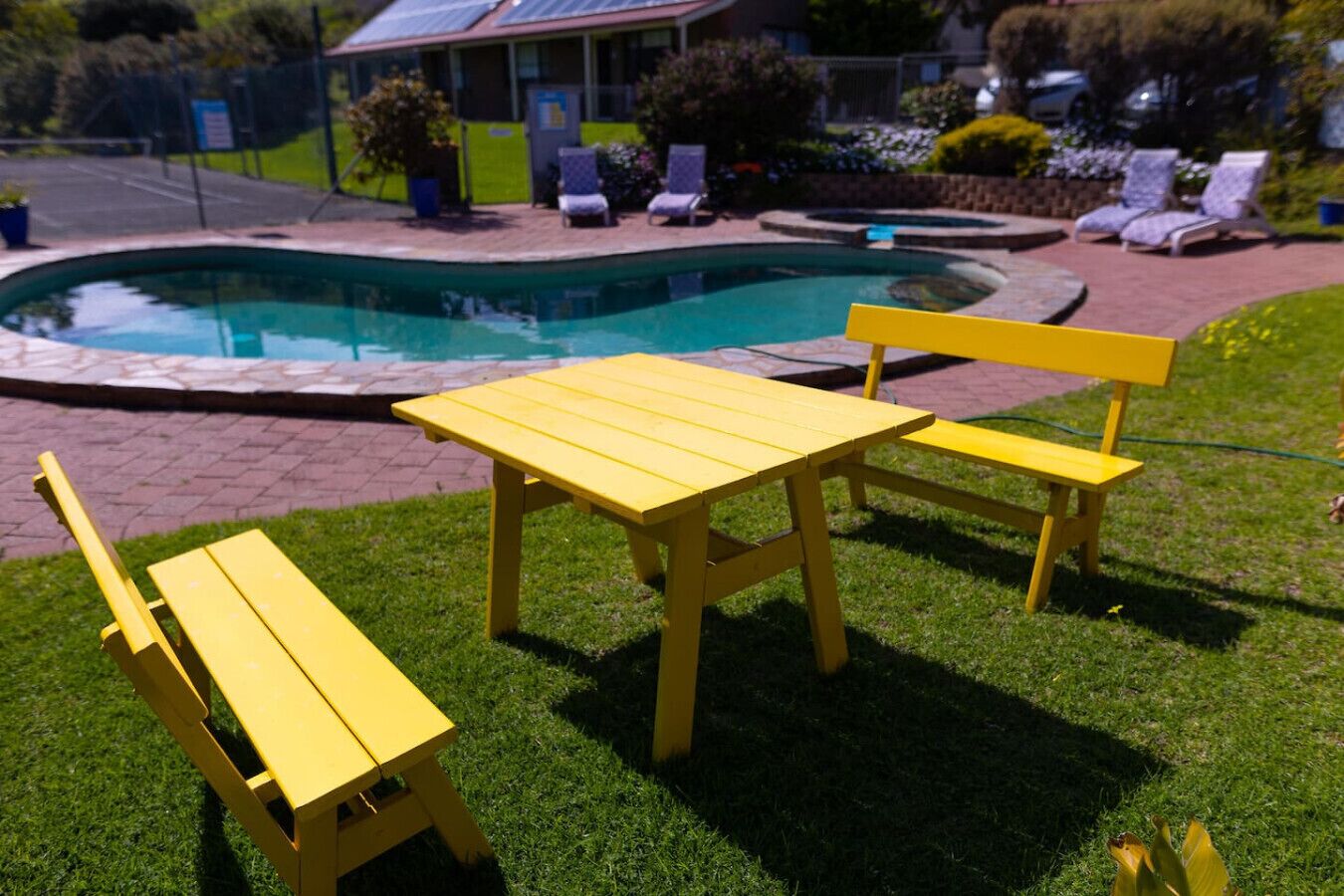 A poolside area with a yellow table and two chairs, surrounded by a well-maintained lawn and a pool.