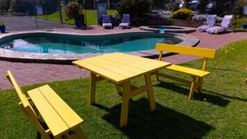 A poolside area with a yellow table and two chairs, surrounded by a well-maintained lawn and a pool.