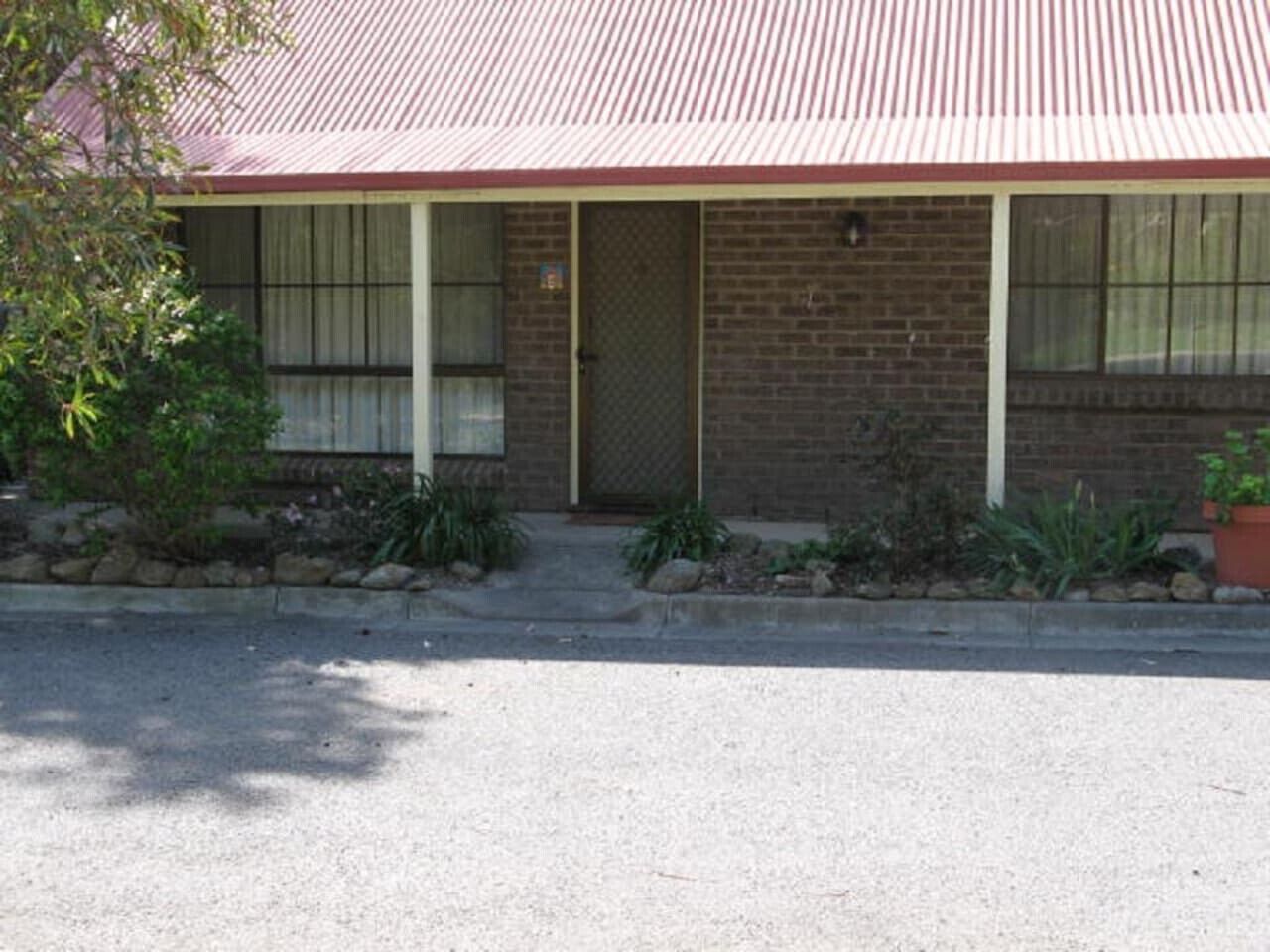 A single-story brick building with a red roof, a front door, and a small porch with steps leading up to it.
