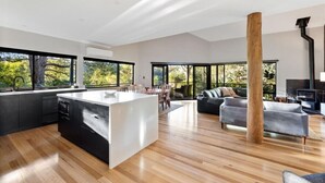 A modern kitchen with a central island, a dining area with chairs, and a living room with a sofa. - Abundance | Sophisticated Luxury | River View (Margaret River)