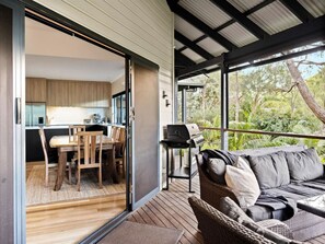 An open-plan living area with a dining table and chairs, a sofa, and a grill outside.