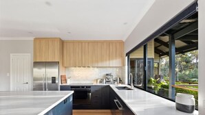 A modern kitchen with a large island, built-in appliances, and a view of the outdoors. - Abundance | Sophisticated Luxury | River View (Margaret River)