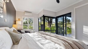 A bedroom with a large bed, a desk, and a view of greenery through a window. - Abundance | Sophisticated Luxury | River View (Margaret River)