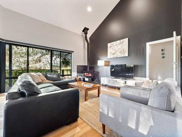 A modern living room with a fireplace, large windows, and a flat-screen TV.
