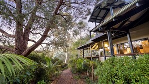 A modern house with a covered porch, surrounded by lush greenery and a large tree. - Abundance | Sophisticated Luxury | River View (Margaret River)