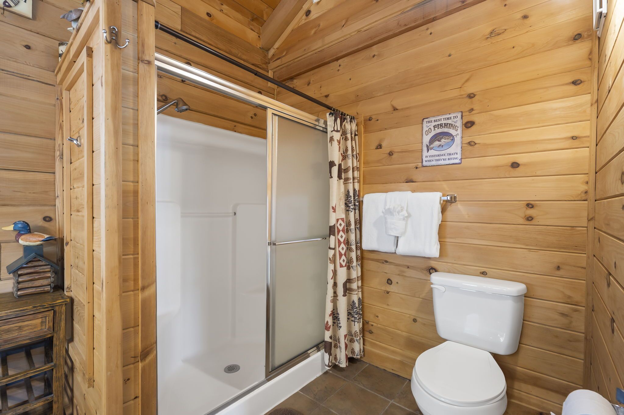 A wooden cabin bathroom with a shower, toilet, and a sign indicating the best time to go fishing.