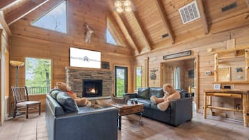A cozy cabin interior with a stone fireplace, leather sofas, and a large bear statue.